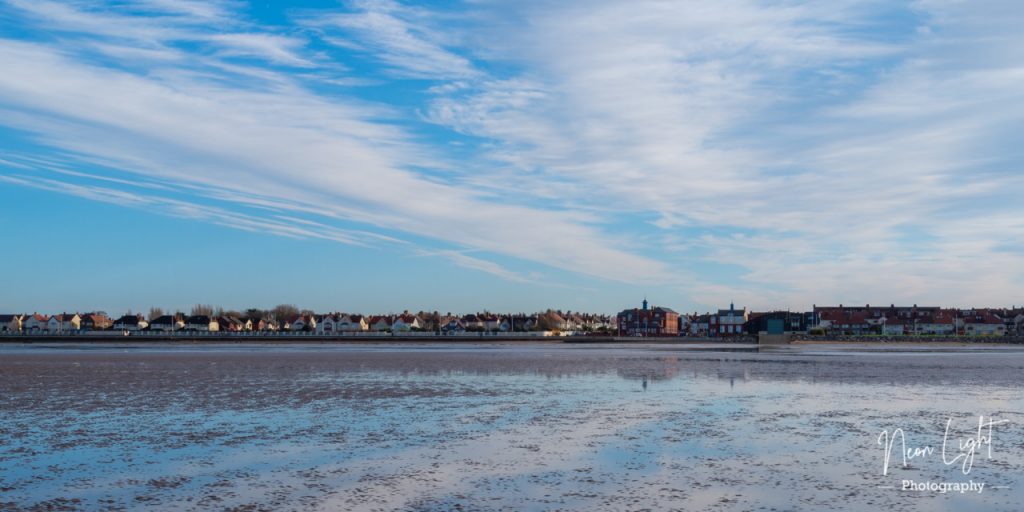A blue winters sky reflects off the wet sand at low tide on Hoylake beach looking back to the Lifeboat Station.